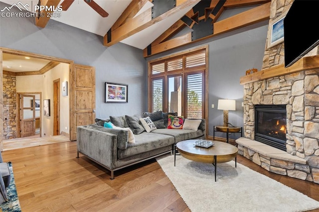 living room featuring high vaulted ceiling, beamed ceiling, light wood-style floors, ceiling fan, and a fireplace