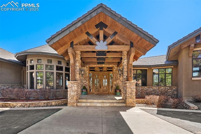 view of exterior entry with a tiled roof, stucco siding, and stone siding