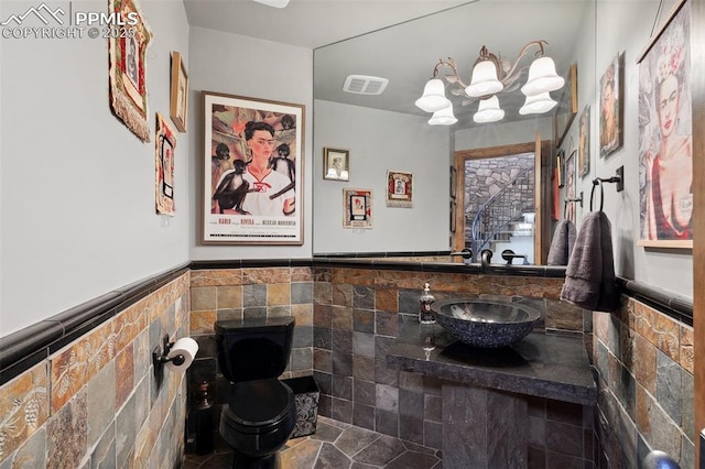 bathroom with a wainscoted wall, visible vents, a notable chandelier, and tile walls