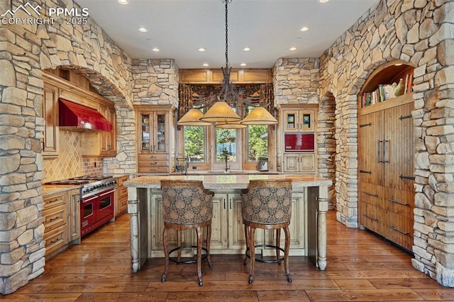kitchen with double oven range, wood-type flooring, a center island, glass insert cabinets, and custom range hood