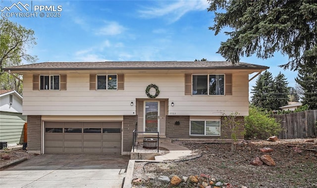 bi-level home featuring brick siding, an attached garage, fence, and concrete driveway