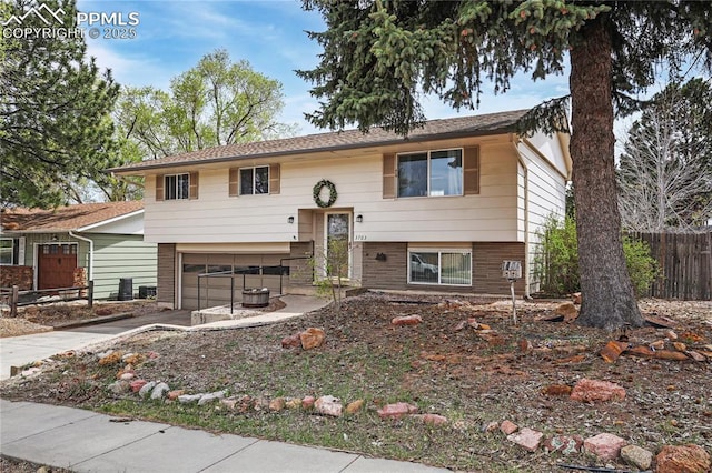 bi-level home with fence, driveway, brick siding, and a garage