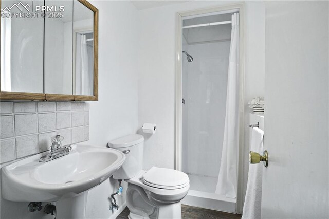 full bath featuring decorative backsplash, a sink, a stall shower, and toilet