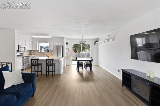 living area featuring baseboards, a textured ceiling, light wood finished floors, and a wealth of natural light