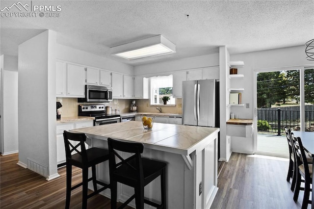 kitchen featuring a kitchen island, stainless steel appliances, dark wood finished floors, and white cabinetry