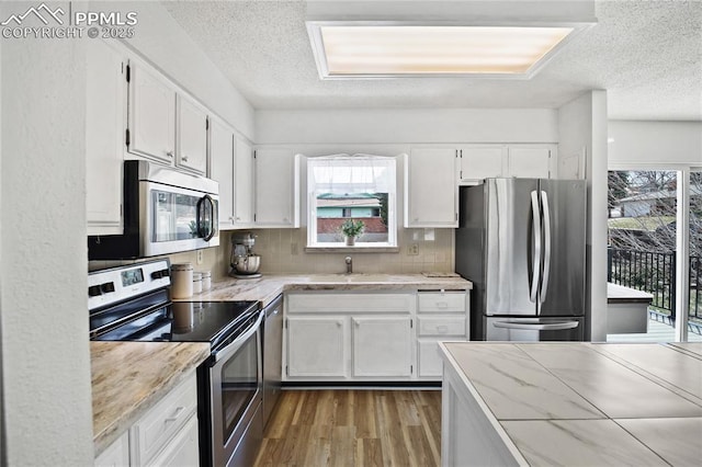 kitchen with stainless steel appliances, white cabinetry, a textured ceiling, and wood finished floors