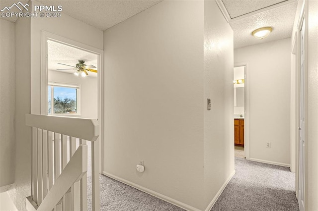 corridor with baseboards, an upstairs landing, light colored carpet, and a textured ceiling