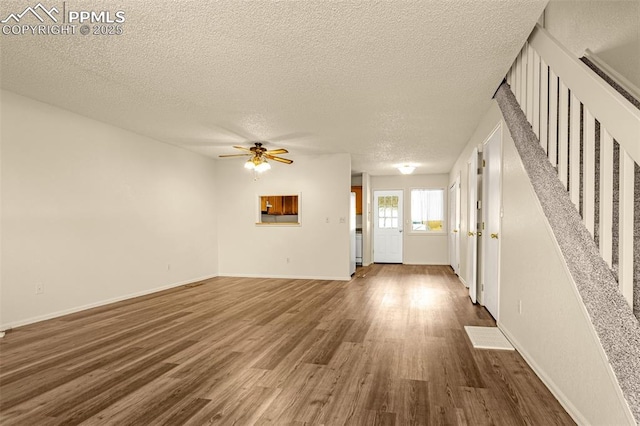 unfurnished living room featuring a textured ceiling, wood finished floors, baseboards, ceiling fan, and stairs