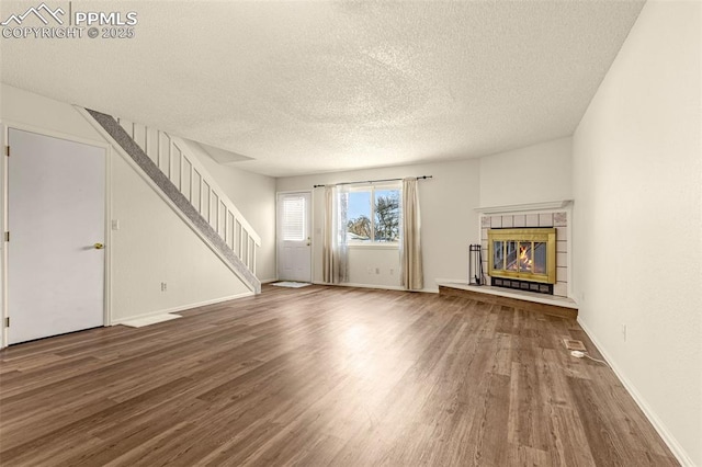 unfurnished living room with a tiled fireplace, stairway, a textured ceiling, and wood finished floors