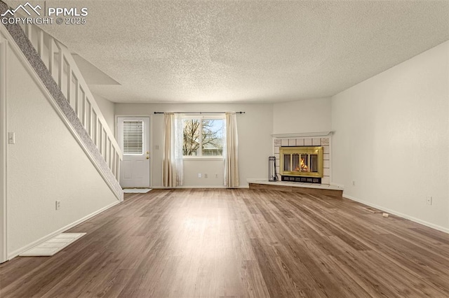 unfurnished living room with a tile fireplace, a textured ceiling, baseboards, and wood finished floors