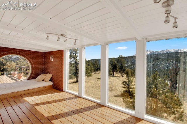 unfurnished sunroom featuring wood-type flooring, wooden ceiling, beam ceiling, and brick wall