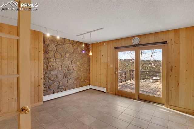 empty room with rail lighting, a textured ceiling, and wood walls