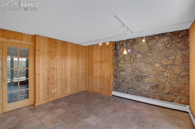 empty room featuring track lighting, a baseboard radiator, a textured ceiling, baseboards, and wooden walls