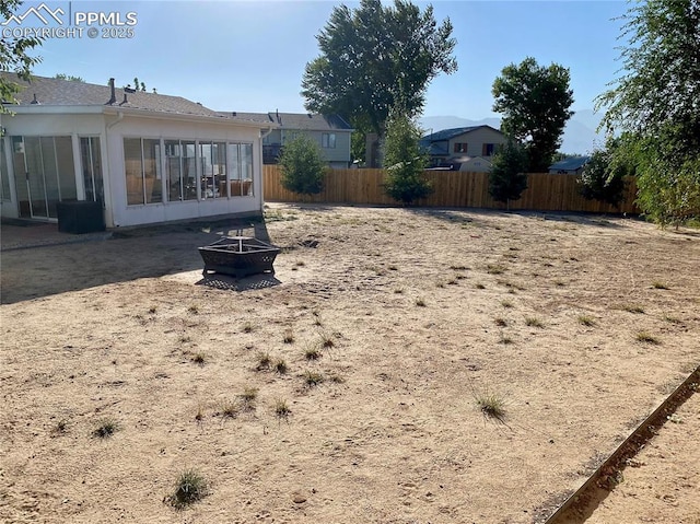 view of yard featuring a sunroom, fence, and an outdoor fire pit
