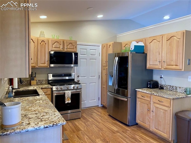 kitchen featuring light stone countertops, light brown cabinets, appliances with stainless steel finishes, and light wood-style floors
