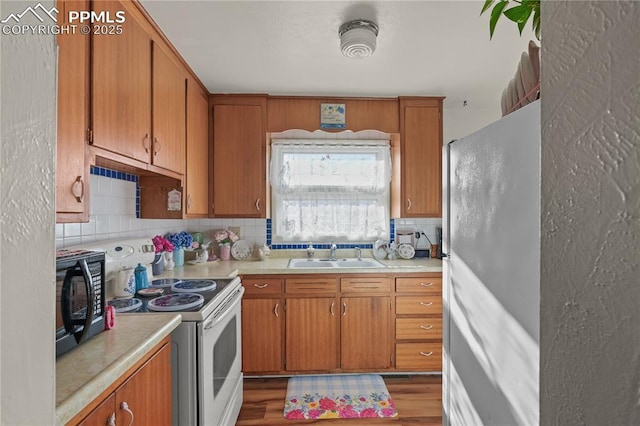 kitchen with brown cabinets, a sink, backsplash, white appliances, and light countertops