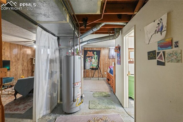 below grade area featuring wooden walls, ceiling fan, and water heater