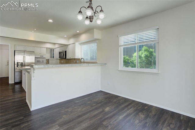 4730 Jenson Ln, Colorado Springs, CO 80922 - kitchen featuring appliances with stainless steel finishes, dark wood-style floors, glass insert cabinets, a peninsula, and a chandelier