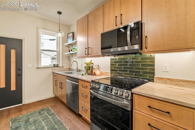 kitchen featuring open shelves, a sink, light wood-style flooring, appliances with stainless steel finishes, and hanging light fixtures