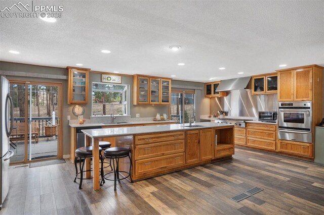 6770 Gun Club Trl, Colorado Springs, CO 80908 - kitchen featuring light countertops, appliances with stainless steel finishes, dark wood-style floors, wall chimney exhaust hood, and a warming drawer