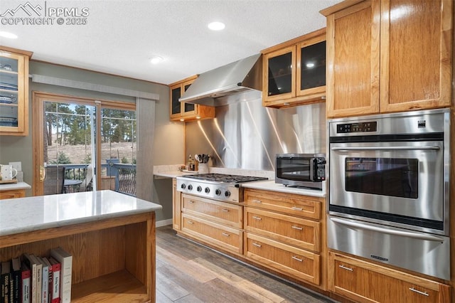 6770 Gun Club Trl, Colorado Springs, CO 80908 - kitchen with light wood finished floors, glass insert cabinets, appliances with stainless steel finishes, a warming drawer, and wall chimney exhaust hood