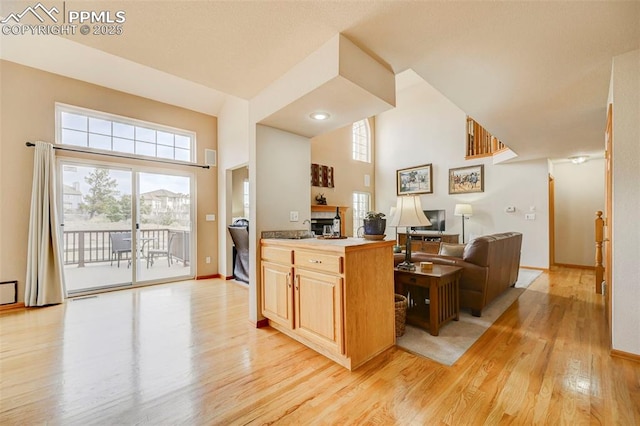 kitchen with baseboards, open floor plan, light wood-style floors, and a towering ceiling