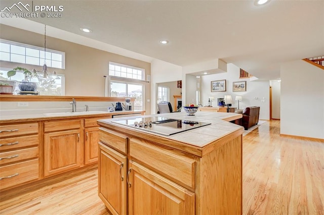 kitchen with black electric stovetop, tile countertops, light wood finished floors, and a sink