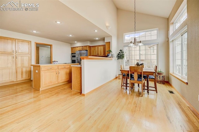 kitchen with high vaulted ceiling, visible vents, a peninsula, stainless steel refrigerator with ice dispenser, and light wood-type flooring
