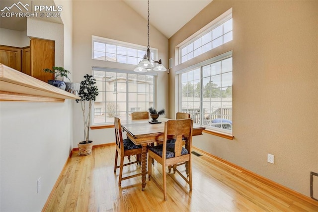 dining room featuring high vaulted ceiling, light wood-style flooring, baseboards, visible vents, and an inviting chandelier