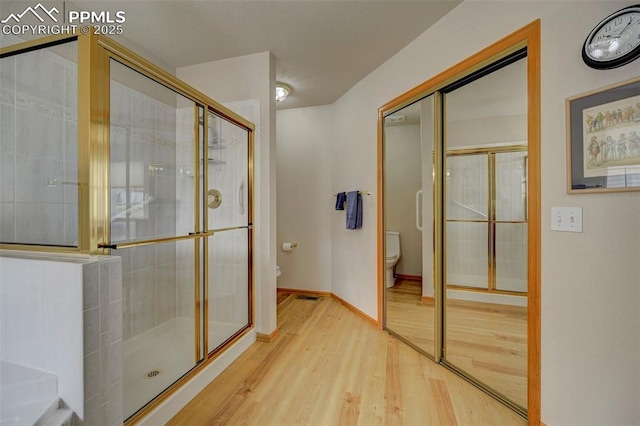 full bath with baseboards, toilet, a shower stall, and wood finished floors