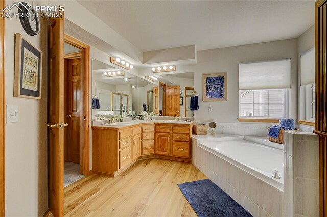 full bath featuring a bath, double vanity, a sink, and wood finished floors