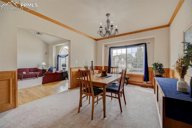 dining room featuring crown molding, vaulted ceiling, light colored carpet, a chandelier, and a wainscoted wall