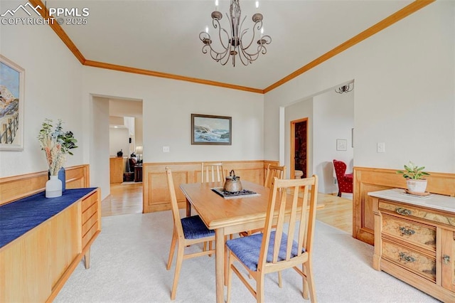 dining room featuring a wainscoted wall, ornamental molding, a notable chandelier, and light colored carpet