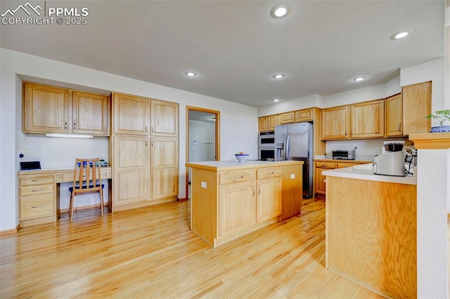 kitchen featuring light countertops, a kitchen island, appliances with stainless steel finishes, light wood-style flooring, and built in desk