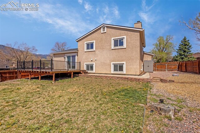 3781 Red Cedar Dr, Colorado Springs, CO 80906 - rear view of house featuring stucco siding, a deck, a fenced backyard, a chimney, and a lawn