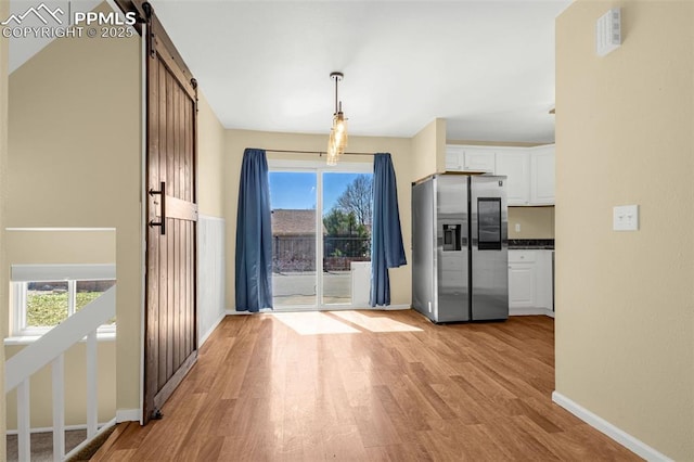 3781 Red Cedar Dr, Colorado Springs, CO 80906 - kitchen featuring a barn door, stainless steel fridge with ice dispenser, light wood-style floors, white cabinetry, and visible vents