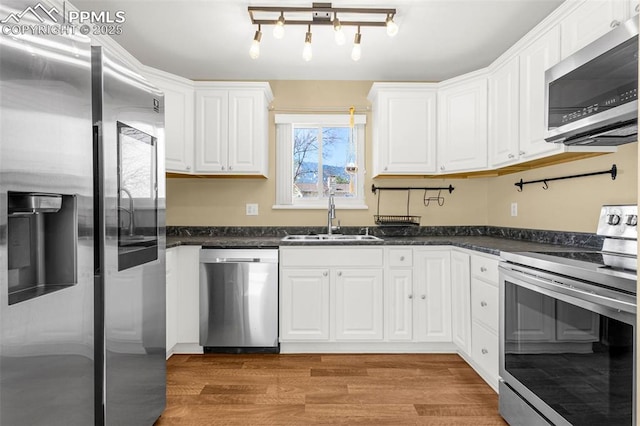 3781 Red Cedar Dr, Colorado Springs, CO 80906 - kitchen featuring appliances with stainless steel finishes, a sink, light wood finished floors, dark stone counters, and white cabinetry