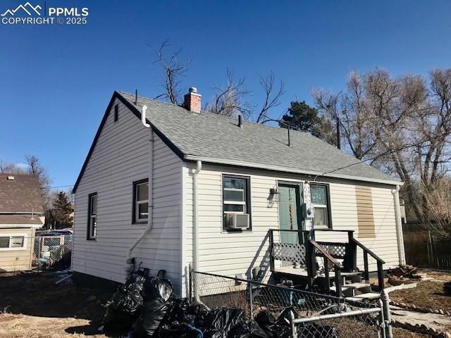 back of house with a shingled roof, a chimney, and fence