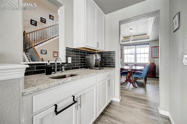 10790 Rolling Peaks Dr, Peyton, CO 80831 - kitchen featuring a sink, a raised ceiling, light wood-style flooring, white cabinets, and decorative backsplash