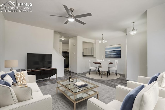 living area with ceiling fan with notable chandelier and wood finished floors
