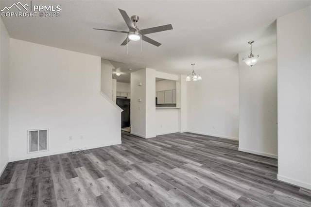 unfurnished living room with wood finished floors, ceiling fan with notable chandelier, baseboards, and visible vents