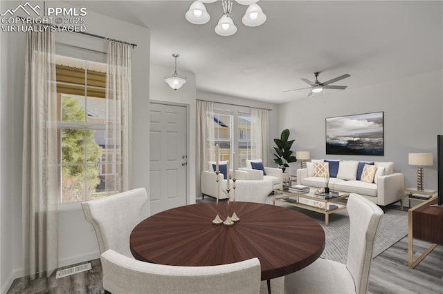 dining area with wood finished floors, ceiling fan with notable chandelier, a healthy amount of sunlight, and visible vents