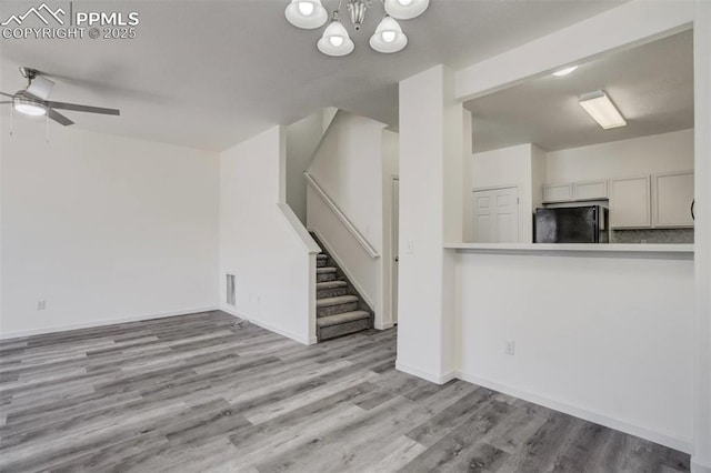 unfurnished living room with baseboards, stairs, wood finished floors, and ceiling fan with notable chandelier