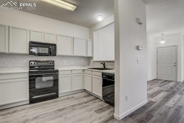 kitchen with light wood finished floors, black appliances, decorative backsplash, and a sink