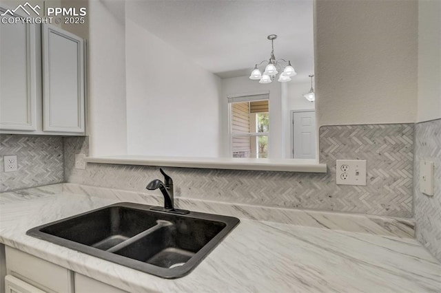 kitchen featuring a notable chandelier, light stone counters, a sink, white cabinetry, and tasteful backsplash