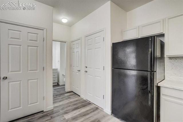 kitchen featuring white cabinets, light wood-style flooring, backsplash, and freestanding refrigerator