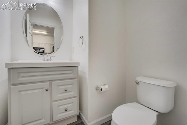 half bath featuring baseboards, toilet, and vanity