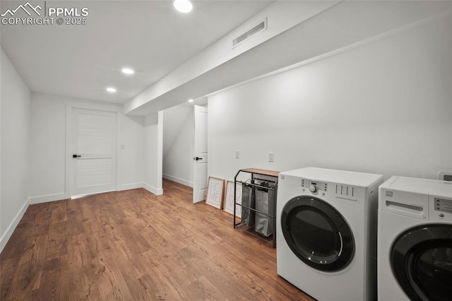 clothes washing area featuring visible vents, baseboards, wood finished floors, laundry area, and washer and clothes dryer