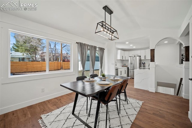 dining area featuring baseboards, a wealth of natural light, wood finished floors, and arched walkways