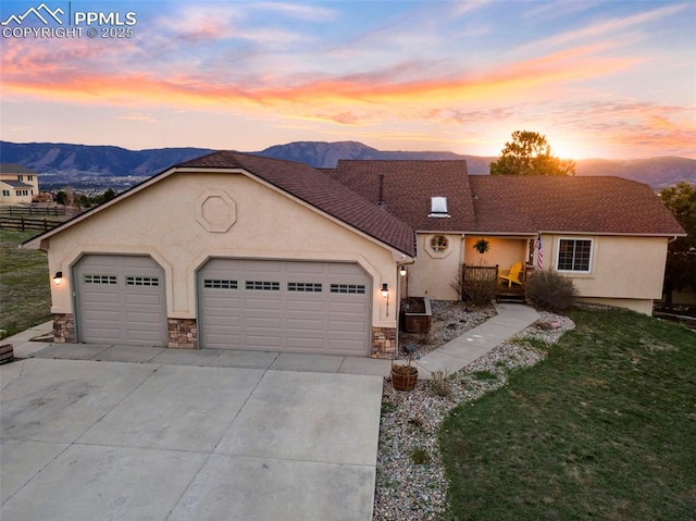 view of front of house with an attached garage, concrete driveway, stucco siding, stone siding, and a mountain view